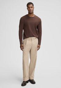 Brązowa koszula z długim rękawem w połączeniu z beżowymi prążkowanymi spodniami. Spodnie mają zapięcie na guzik i zamek błyskawiczny, do kompletu ciemne buty.