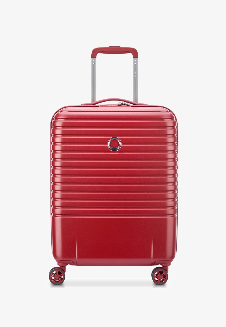 Valigia rigida rossa con scanalature verticali, manico retrattile e quattro ruote girevoli. Presenta un logo metallico e chiusura con zip.