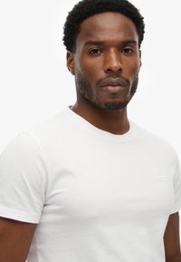 Biała koszulka z krótkim rękawem, wykonana z bawełny, z okrągłym dekoltem; posiada małe haftowane logo na lewej stronie klatki piersiowej.