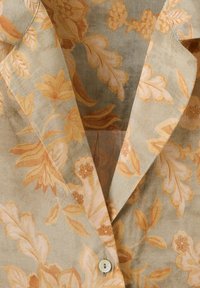 Blazer beige avec un motif floral orange comprenant des feuilles et des fleurs, fermeture à un bouton et revers crantés.