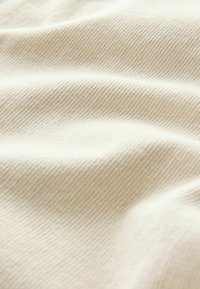 Crème-kleurige stof met een zachte, textuurribbelstructuur, uitgerust met subtiele golfachtige plooien en een egale afwerking.