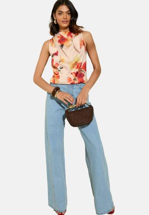Top senza maniche con stampa floreale in morbido tessuto, abbinato a jeans a gamba larga blu chiaro. Il modello tiene una piccola borsa intrecciata, con manico dorato.