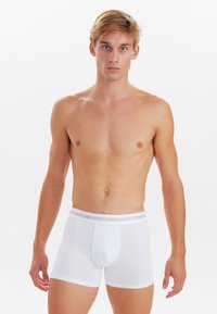 Boxer briefs in cotone bianco con una texture morbida, cintura elastica con il nome del marchio stampato e una forma aderente, esposti su uno sfondo neutro.