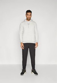 Γκρι φούτερ με κορδόνια, σε συνδυασμό με μαύρο αθλητικό παντελόνι και μαύρα αθλητικά παπούτσια με πράσινες λεπτομέρειες, σε απλό φόντο.