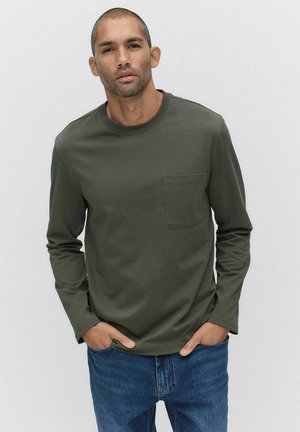 Langdynamische shirt in donkergroen, met een ronde hals en een borstzak, gecombineerd met blauwe denim jeans. Zachte stoftextuur.