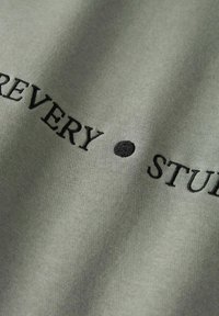 Groen katoenen stof met zwarte geborduurde tekst waarop "EVERY" en "STUDY" staan, met een zwarte vaste stip ertussen.