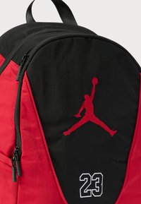 Μαύρο και κόκκινο σακίδιο πλάτης με κόκκινη σιλουέτα λογότυπου Jordan και λευκό κεντημένο αριθμό 23 στην μπροστινή τσέπη.