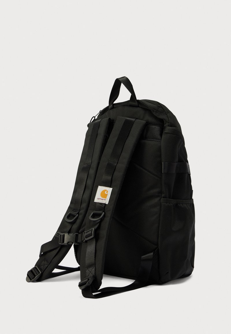 Black fabric backpack with adjustable padded straps, a top handle, side pockets, and a logo patch. Features a structured, rectangular shape.