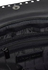 Interno di una borsa nera in pelle con una tasca con zip, fodera morbida e un'etichetta. L'esterno presenta fori decorativi lungo il bordo.