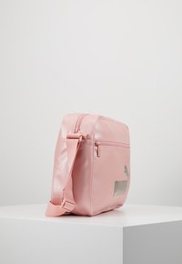Borsa sintetica rosa con tracolla regolabile, forma rettangolare, tasca con cerniera frontale e logo "PUMA" grigio sul lato.