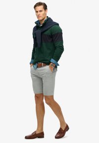 Groen en marineblauw kleur geblokte trui laag over een spijkerhemd, gecombineerd met lichtgrijze shorts en bruine instapschoenen. Accessoires omvatten een horloge.