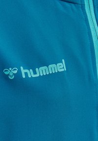 Chaqueta deportiva en color turquesa con cremallera azul claro y logo. Confeccionada en tela suave, presenta un logo en el área del pecho.
