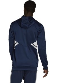 Felpa atletica navy con una consistenza testurizzata, cappuccio e strisce bianche di accento sulla schiena, caratterizzata da un design geometrico e polsini aderenti.