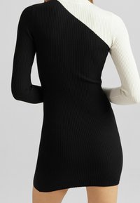 Robe pull côtelée à manches longues ; présente un corps noir et un empiècement blanc sur l'épaule, mettant en avant un design à couleurs contrastées.
