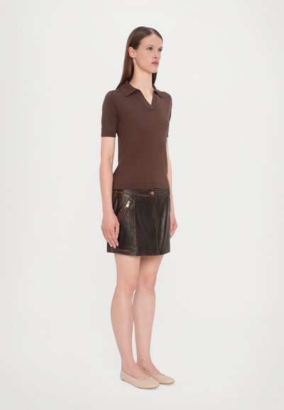 Polo-shirt marron à manches courtes avec un col en V, associé à une jupe en cuir noire dotée de poches zippées et d'accents de couture marron.