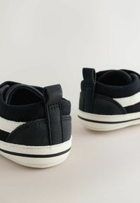 Black canvas shoes with a white stripe, rounded toe, and reinforced heel. Features a textured finish and a pull tab at the back.