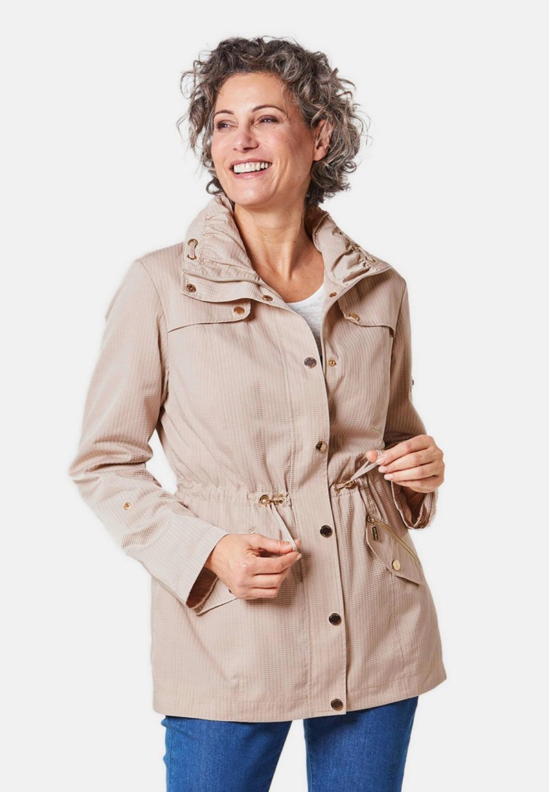 Beige, textuurjasje met een hoge kraag, een taille met trekkoord en knoopaccenten. Beschikt over twee zijzakken. Geschikt voor casual wear.
