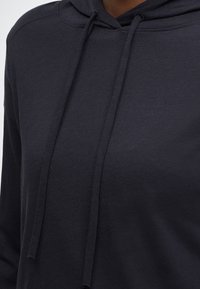 Tmavo sivá mikina s kapucňou na šnúrku, vyrobená z mäkkej, textúrovanej látky. Má klasický dizajn kapucne a voľný strih.