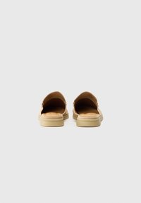 Tan slip-on shoes with an open back, cushioned insole, rounded toe, and minimalistic design. Soft suede material and beige sole.