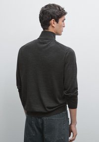 Dark gray sweater with a high collar, fitted design, and ribbed cuffs. Worn over dark denim jeans, shown from the back.