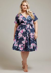 Vestido envolvente floral en tejido azul marino con mangas cortas, un lazo en la cintura y rosas rosas con hojas verdes. Textura suave, hasta la rodilla.