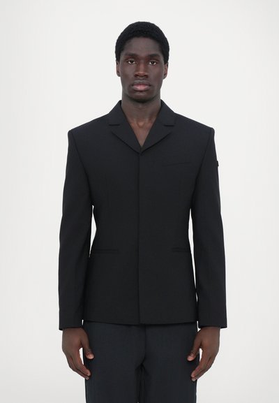 Sort skræddersyet jakkesæt med notch lapel, en enkelt lomme og strukturerede skuldre. Glat stof og klare linjer; minimalistisk design.