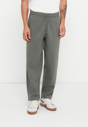 Donkergroene trainingsbroek met een elastische tailleband en trekkoord, voorzien van zijzakken en een relaxte pasvorm, gecombineerd met witte sneakers.