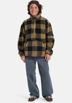 Sudadera de fleece con patrón de cuadros amarillos y negros, con media cremallera, bolsillo frontal y tejido texturizado. Combinada con pantalones grises holgados.
