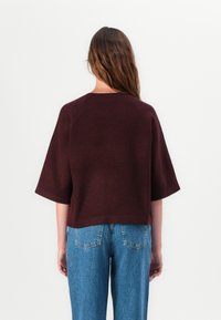 Bordeaux strikket topp med en avslappet silhuett og korte ermer, kombinert med lyseblå vide jeans. Glatt tekstur, minimalistisk design.