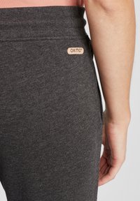 Dunkelgraue Leggings mit einer weichen Textur, ausgestattet mit einem gerippten Taillenbund und einem angenähten, hellbraunen Markenetikett auf der Rückseite.