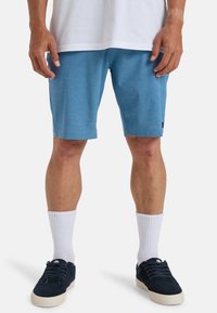 Blauwe sportshorts van een lichte stof, met een gladde textuur en zijzakken, gecombineerd met witte crew-sokken en donkere sneakers.