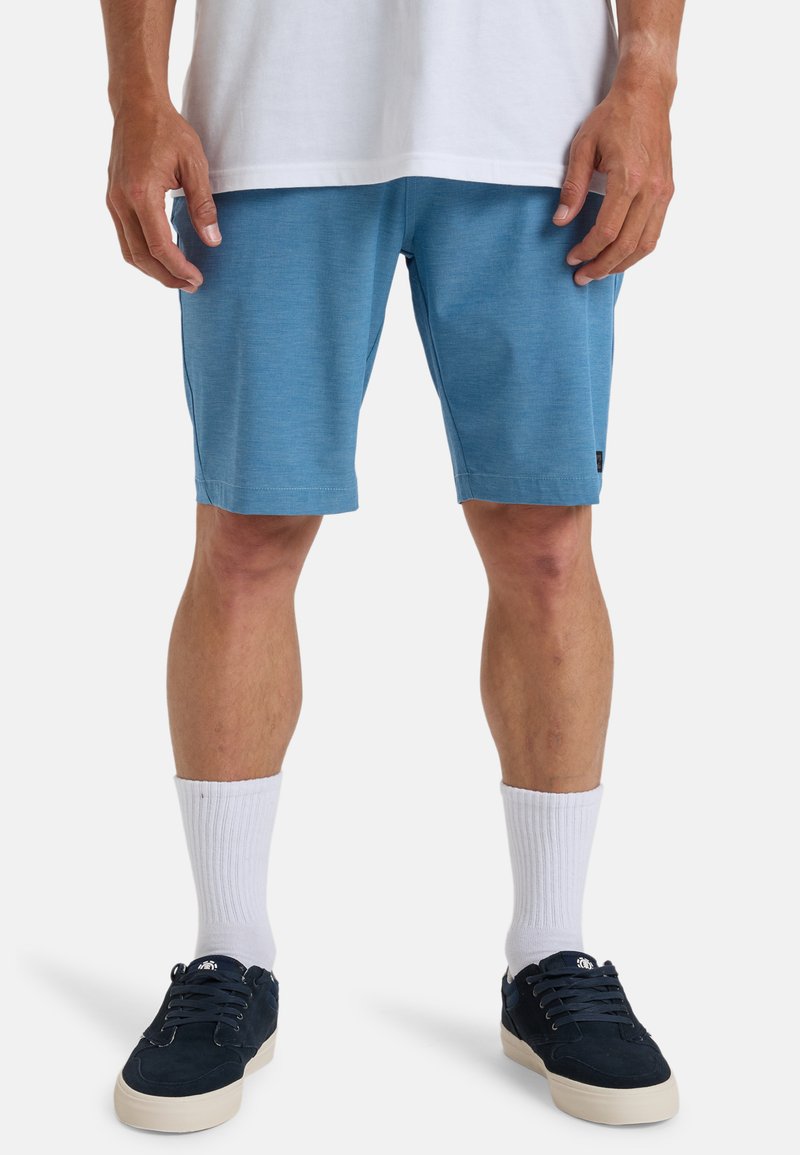 Blauwe sportshorts van een lichte stof, met een gladde textuur en zijzakken, gecombineerd met witte crew-sokken en donkere sneakers.