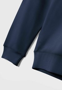 Sweatshirt bleu marine avec des poignets et un ourlet côtes, présentant une texture lisse et un col ras du cou, montrant une partie de la manche et du corps.