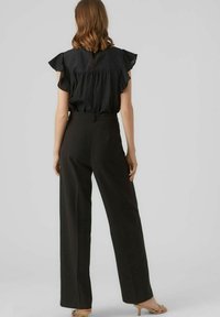Sort peplum-top med voluminøse ærmer, parret med højtaljede sorte wide-leg bukser. Glat texture og minimalistisk design.