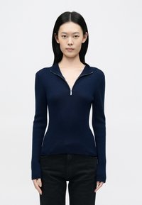 Tengerészkék bordázott pulóver cipzáras gallérral és hosszú ujjakkal, testhezálló sziluett, texturált kötés és minimalista dizájn.