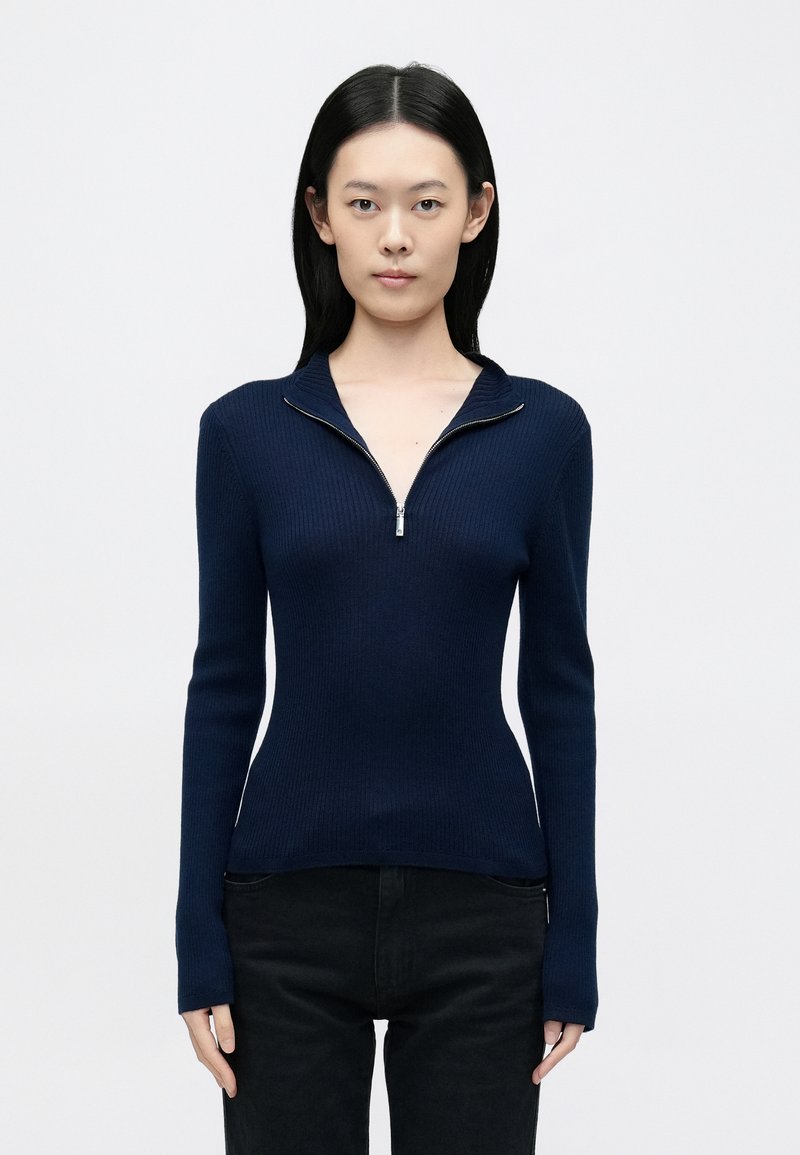 Tengerészkék bordázott pulóver cipzáras gallérral és hosszú ujjakkal, testhezálló sziluett, texturált kötés és minimalista dizájn.