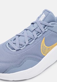 Zapatilla deportiva de malla azul claro con suela blanca, con el logotipo de Nike en amarillo, superficie texturizada y cordones planos.
