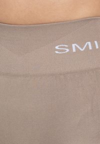 Beige geribde tailleband met het woord "SMIL" in witte letters. Effen textuur met een aansluitend ontwerp, ideaal voor sportkleding of loungekleding.