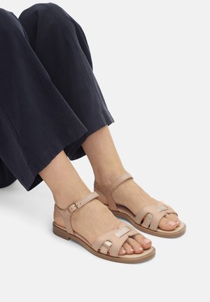 Jasnoróżowe sandały z odkrytymi palcami, regulowanym paskiem wokół kostki, gładką skórzaną powierzchnią oraz metalicznymi akcentami na przodzie. Płaska podeszwa.