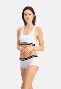 Sujetador deportivo blanco de algodón y bragas cortas con una banda elástica de marca negra. Textura suave, diseño deportivo y estilo de espalda nadadora.