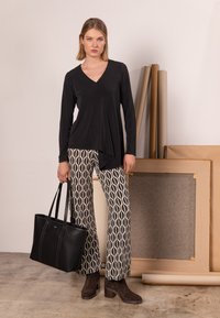 Schwarzes Langarm-Oberteil mit V-Ausschnitt, kombiniert mit gemusterten, weit geschnittenen Hosen in Creme und Marineblau. Accessoires umfassen eine schwarze Tragetasche und braune Stiefeletten.