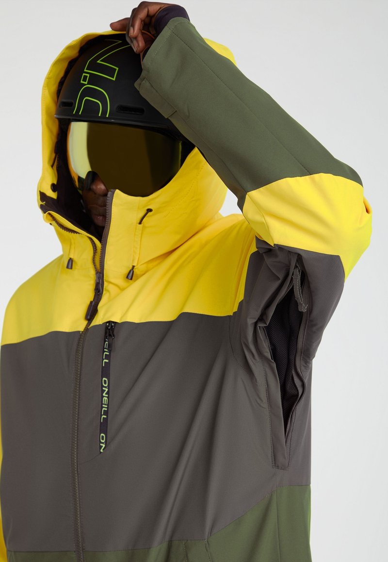 Żółto-szara ocieplana kurtka z kapturem, z zapięciem na zamek z przodu, z kolorowymi sekcjami oraz regulowanymi detalami na mankietach.