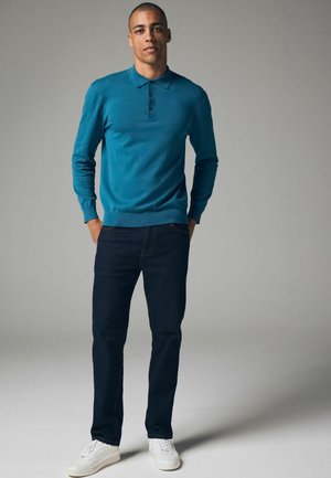 Több színben kapható hosszú ujjú, teal színű póló, három gombbal, sötétkék farmernadrággal és fehér sportcipővel párosítva. Simább textúra, laza szabás.