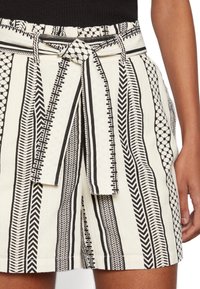 Shorts à motifs noir et blanc avec des rayures verticales, dotés d'une taille nouée et de divers motifs géométriques. Confectionnés en tissu léger.