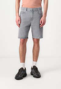 Grå denimshorts med rett snitt, som har fem lommer, knappelukking og synlige sømmer. Kombinert med mørke joggesko og hvite sokker.