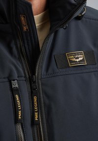 Tamno plava jakna s visokim ovratnikom, dvostrukim patentnim zatvaračima i tekstilnim aplikacijama s natpisom "PME LEGEND". Glatka tekstura s modernim dizajnom.
