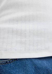 Tessuto a righe bianche con linee verticali e piccoli fori, abbinato a jeans in denim blu, che mostrano texture e sovrapposizione.