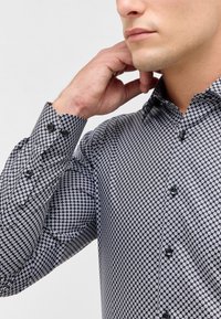 Camicia da uomo a maniche lunghe con motivo bianco e nero, dal design fitted, con colletto a punta e bottoni neri sui polsini e sul davanti.