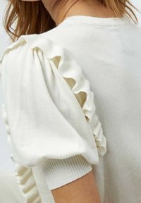 Krämfärgad tröja med korta, puffiga ärmar som har rynkade detaljer. Tyget är mjukt och texturerat, med en ribbad manschettaccent.