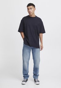 Navy blue oversized t-shirt with a pocket, paired with light blue jeans and black and white patterned sneakers. Solid colors, casual fit.